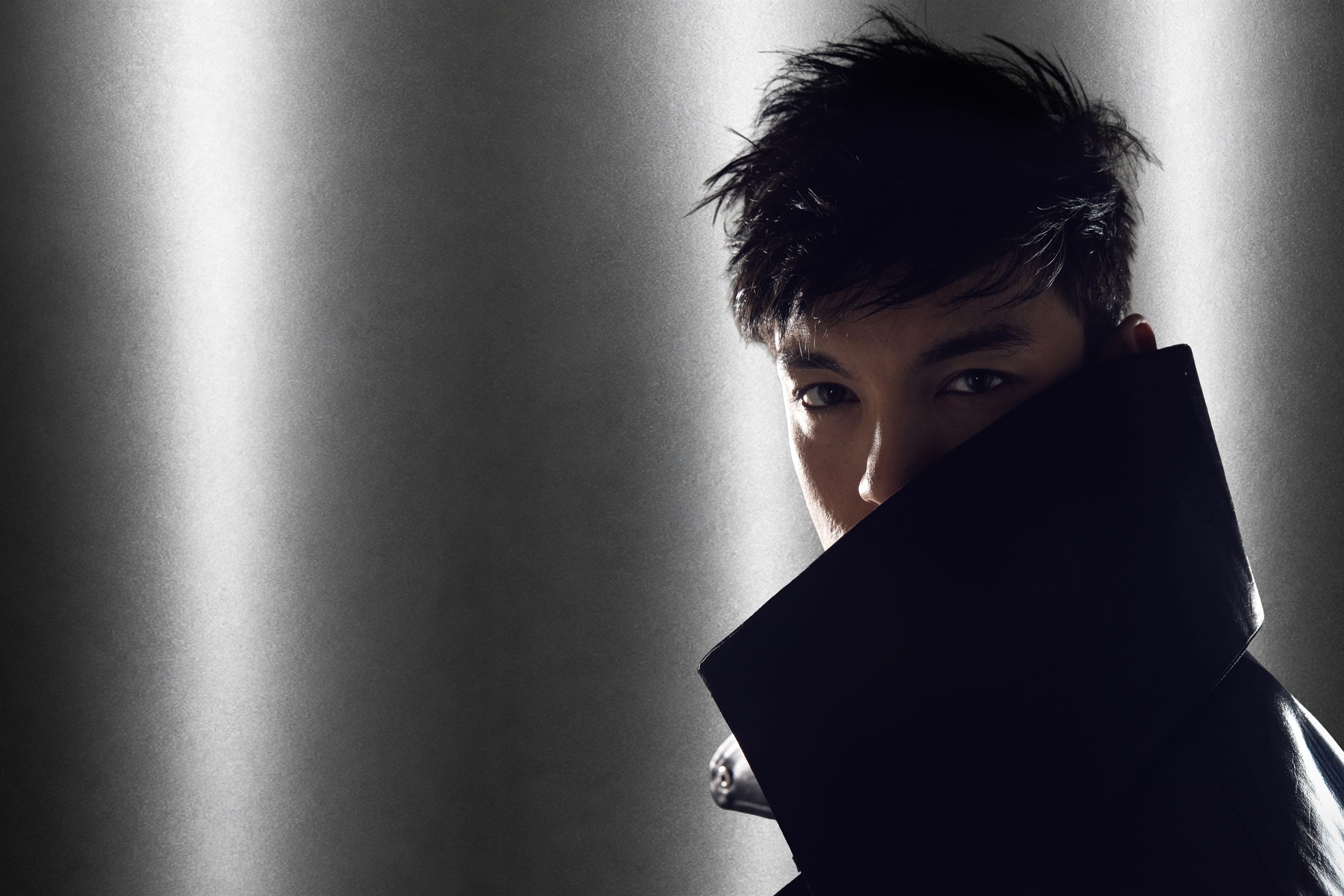 Editorial portrait of a model against a silver metallic backdrop, lower face concealed behind a dark collar